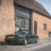 A rear right side shot of a dark green Mazda MX 5 parked outside a farm building