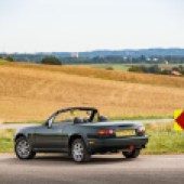 A rear left side shot of a green Mazda MX 5 with a brown field background