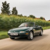 A front left side driving shot of a dark green Mazda MX 5