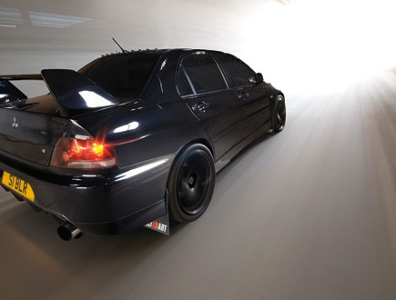 A rear right side shot of a black Mitsubishi Lancer Evolution driving out of a tunnel