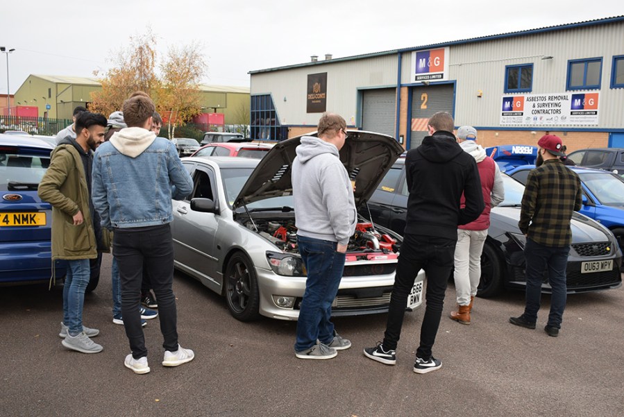 A group of people checking out the engine bay of a Lexus.