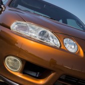 A close up of the front right headlight of an orange Lexus Soarer Z30
