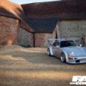 A red brick building with the right side of a silver Porsche 964