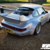 A rear right corner shot of a silver Porsche 964 parked on gravel