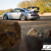 A pile of unfocused logs with a focused view of the left side of a Porsche 964