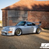 Sun shining on the tile roof of a farm building behind a silver Porsche 964
