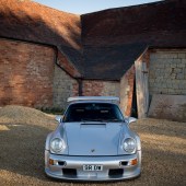 A front view of a silver Porsche 964 with a brick building backdrop