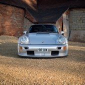 A low central shot of a Porsche 964 parked on gravel