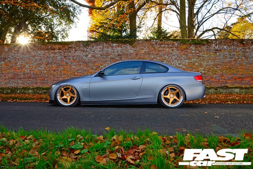 Matte silver BMW-335I-E92 with gold rims and a red brick backdrop