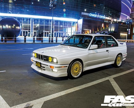 A front left side shot of a white BMW E30 M3 with gold detailing at night