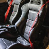 A shot of the black leather seats and red seatbelts inside a BMW E30 M3