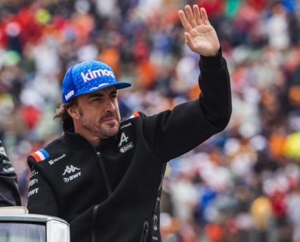 Fernando Alonso in a blue cap and black jacket, waving to the crowds
