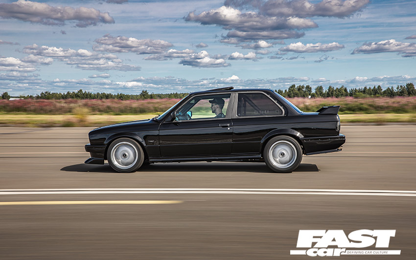 Side-profile driving shot of black modified BMW E30 turbo