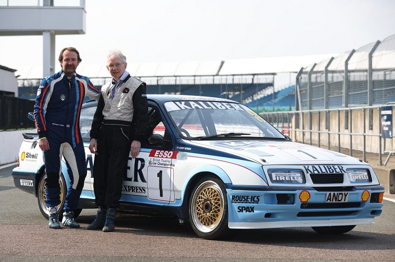 Two men leaning against the right side of a Rouse Ford Sierra RS500 on a racetrack