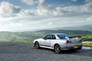 A Nissan Skyline GT-R R34 looking out over a mountainous landscape. 
