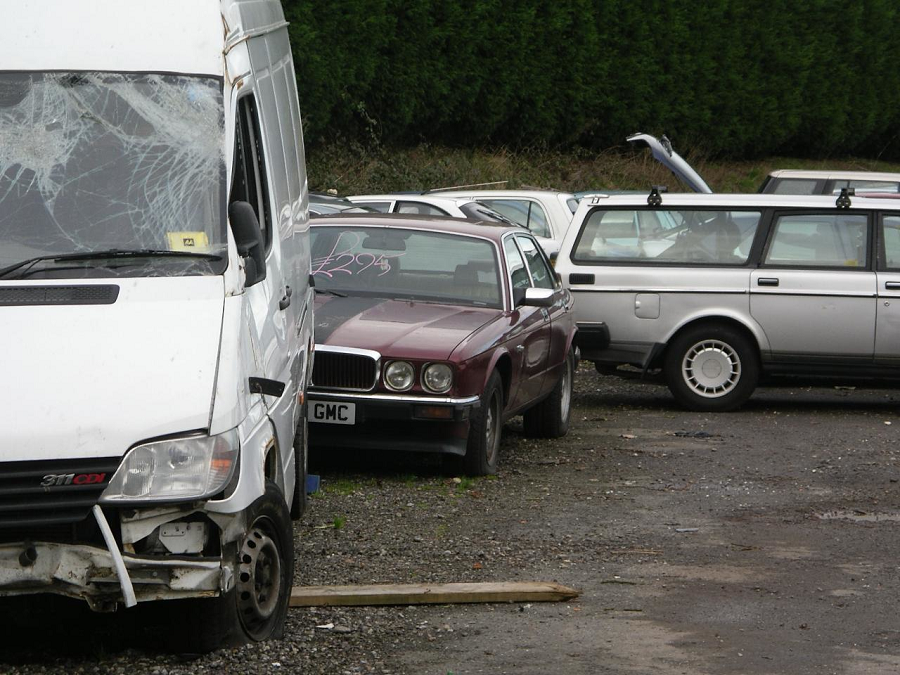 A scrapped Jaguar in between a Mercedes van and a Volvo.
