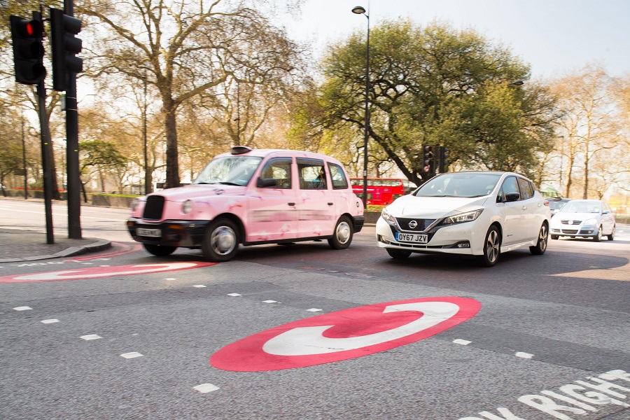 A taxi and a Nissan Leaf driving through London.