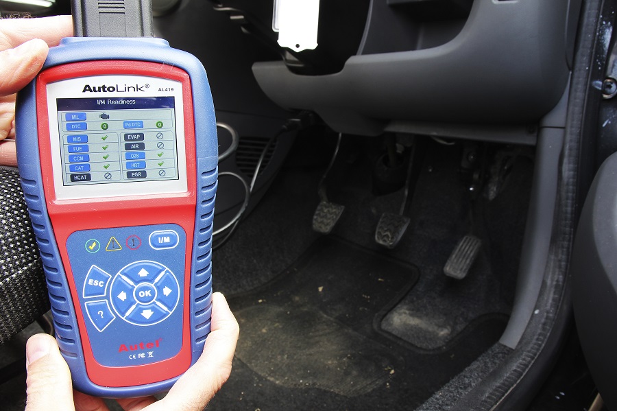 A fault code reader being held near a car's footwell.