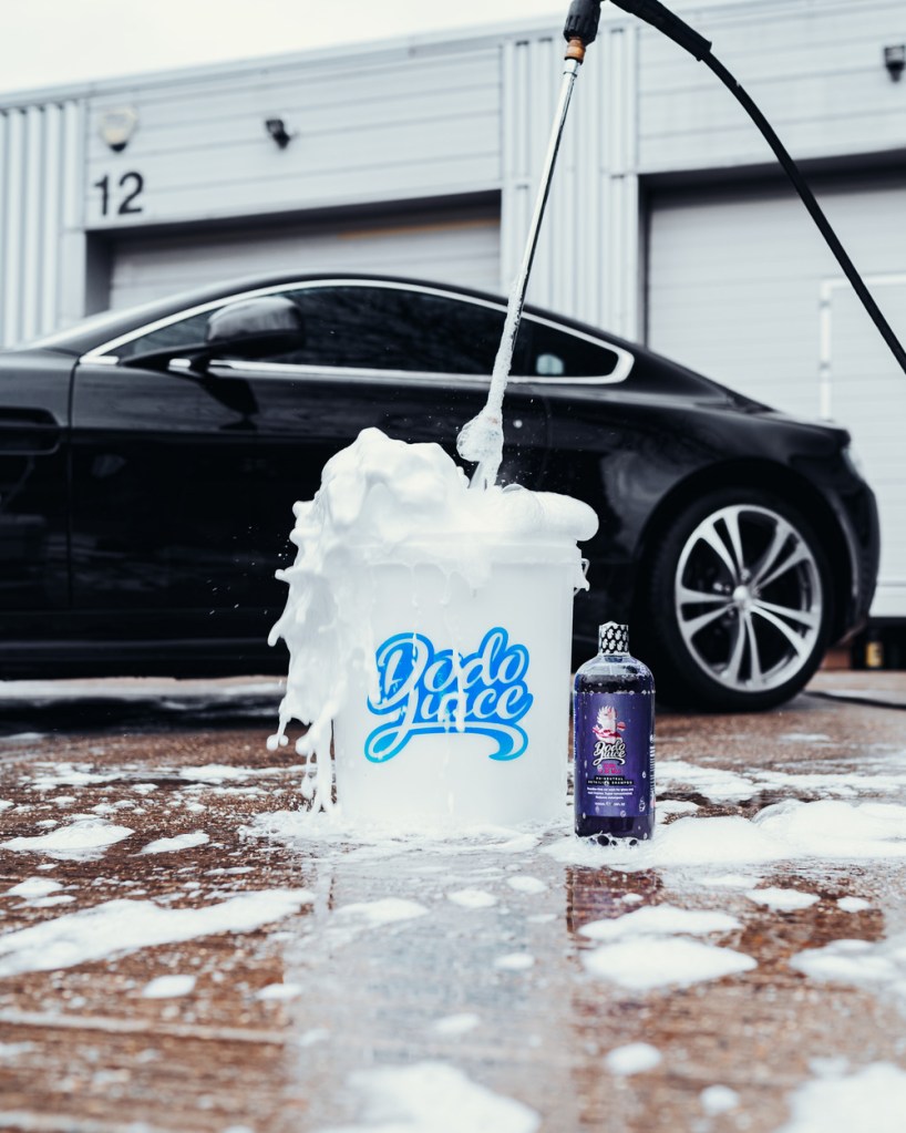 foaming bucket of car shampoo with car in the background
