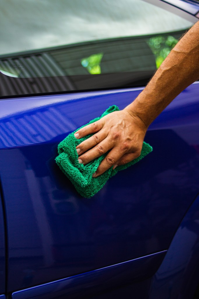 man holding microfibre cloth and buffing clean a car's paintwork