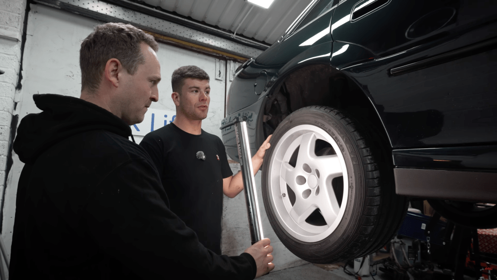 Two men inspect the wheels of a Lotus Carlton on a ramp