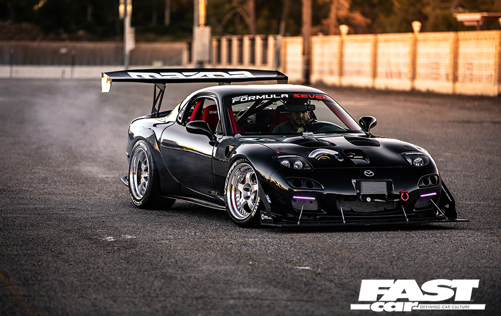 A front right side shot of a black Rotor Mazda RX 7 driving