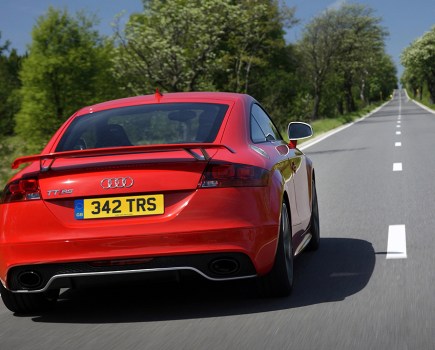 Behind view of a red Audi TT driving down straight grey road