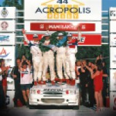 A team holding winners wreaths, standing on the bonnet of an Escort Cosworth WRC