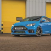 A front left shot of a bright blue Ford Focus RS Mk3 in front of yellow garage doors