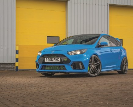A front left shot of a bright blue Ford Focus RS Mk3 in front of yellow garage doors