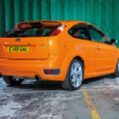 A rear right side shot of an orange Ford Focus ST Mk2 with a green garage door behind