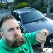 A man in a green hooded jumper putting a thumbs down in front of an Audi RS4 B7 Avant in dark grey