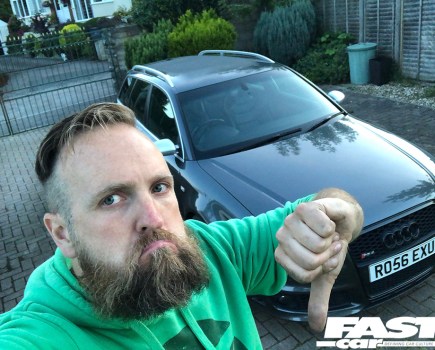 A man in a green hooded jumper putting a thumbs down in front of an Audi RS4 B7 Avant in dark grey