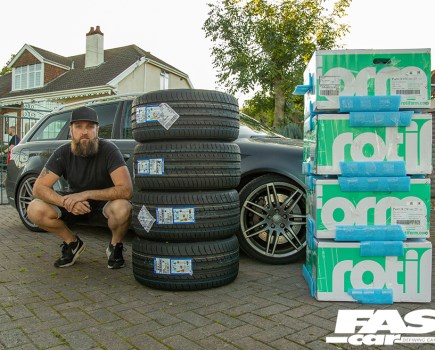 A man in a black cap sqautted next to stack of four tyres with Audi rs4 b7 avant behind