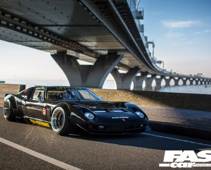 A front right side view of a black Lamborghini Miura driving under a bridge