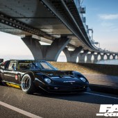 A front right side view of a black Lamborghini Miura driving under a bridge