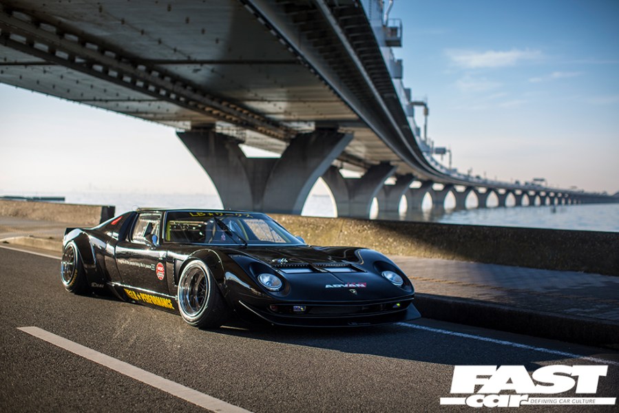 A front right side view of a black Lamborghini Miura driving under a bridge