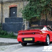 A rear shot of a red Mitsubishi 3000 GT parked in front of a stone building