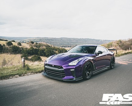 A front left shot of a purple Nissan GT R driving on a country road