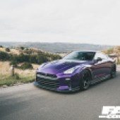 A front left shot of a purple Nissan GT R driving on a country road