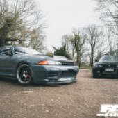 A grey Nissan Skyline GT R parked next to a black Nissan GT R in a forest car park