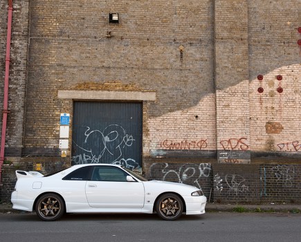 Right side shot of a white Nissan Skyline GT R R33 with red brick backdrop