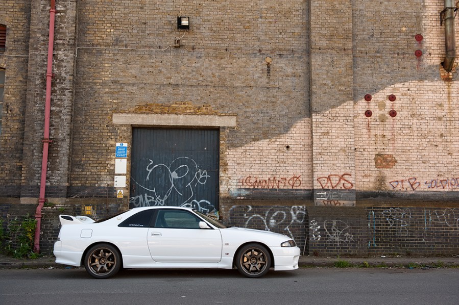 Right side shot of a white Nissan Skyline GT R R33 with red brick backdrop