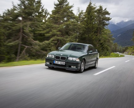 A right left side shot of a dark green BMW M3 driving in the mountains