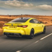 A right rear shot of a yellow BMW M3 driving on a desert road