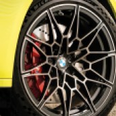 A close up of the back left wheel of a yellow BMW with black alloys