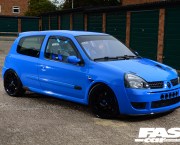A right side shot of a bright blue tuned Renault Clio 182 parked outside some residential garages