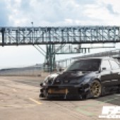 Front left shot of a black Hawkeye Impreza parked on an empty racetrack with gold alloys