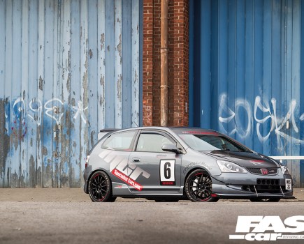 A right side shot of a grey Honda Civic Type R covered in stickers and parked in front of blue garage doors